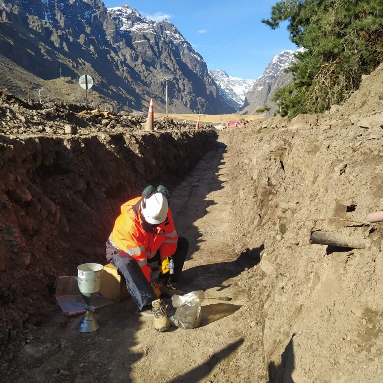 Técnico con el equipo de cono de arena dentro de una zanja, con la cordillera nevada al fondo